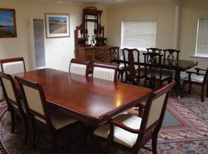 A dining room with a large wooden table surrounded by chairs, a window with blinds, and a decorative rug.