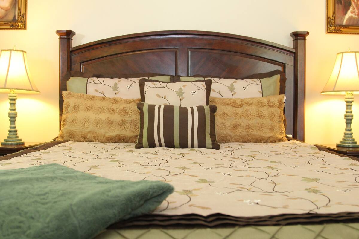 A neatly made bed with a floral-patterned bedspread, two pillows with different designs, and a green throw blanket.