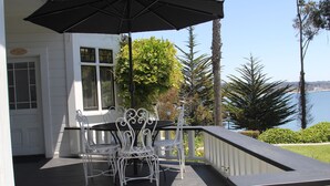 A covered outdoor patio with a table and chairs, a black umbrella, and a view of the sea.