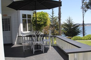 A covered outdoor patio with a table and chairs, a black umbrella, and a view of the sea.