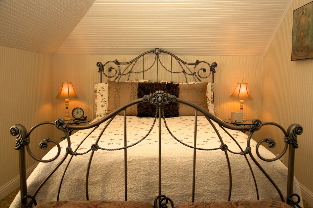 A bed with a metal frame, two bedside lamps, a clock, and a floral-patterned pillow.