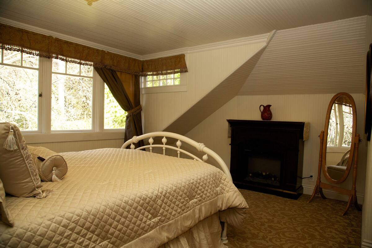 A bedroom with a bed, a fireplace, a mirror, and a window with curtains.