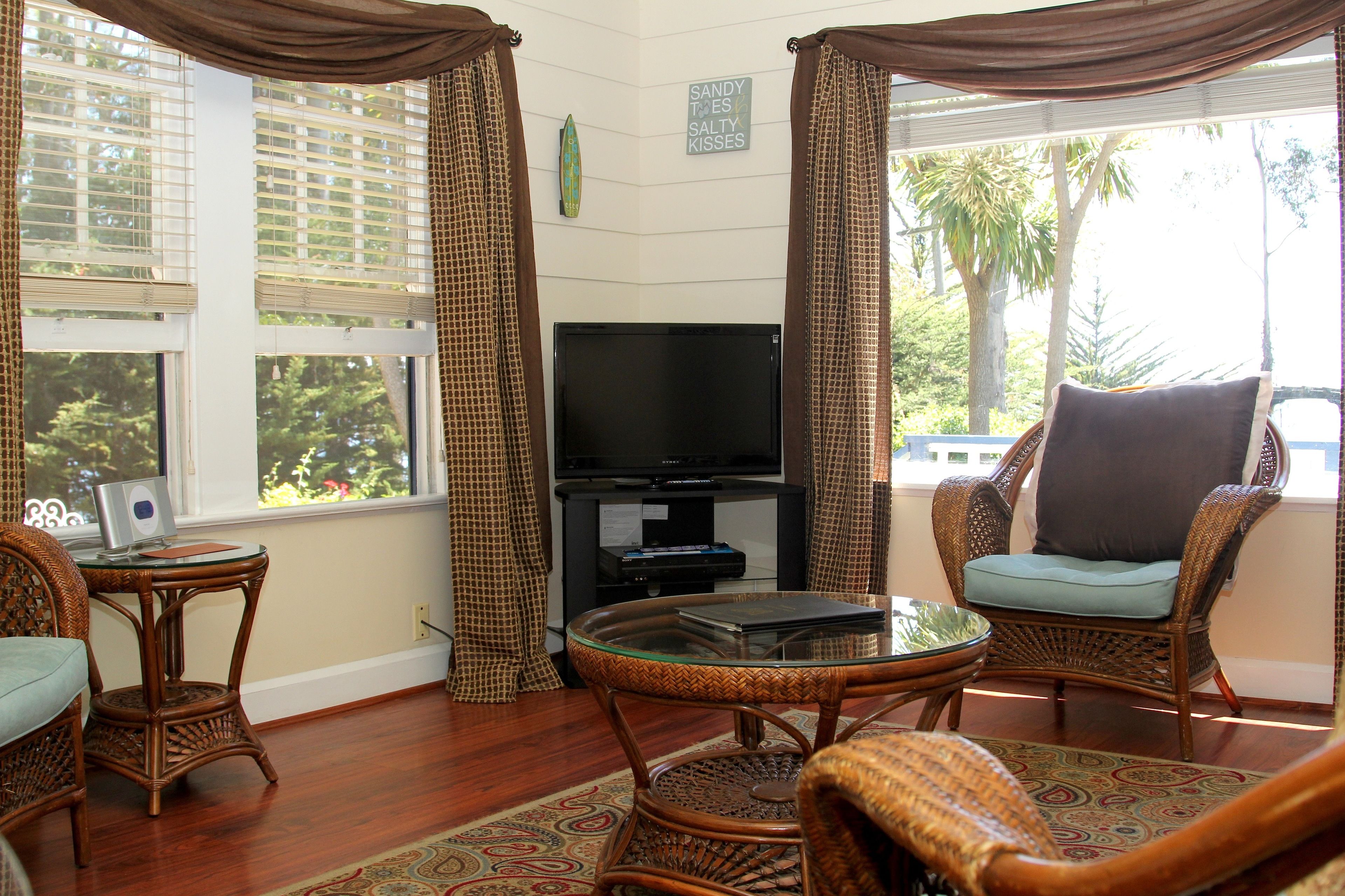 A living room with a television, wicker furniture, and a view of trees.