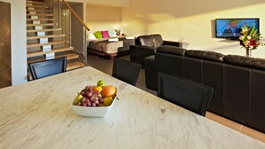 Una sala de estar moderna con un sofá, una mesa de comedor con un frutero, un televisor y una escalera.
