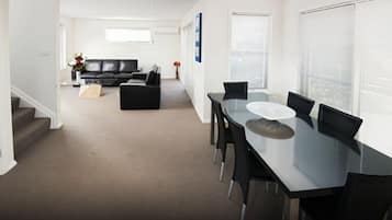 Una sala moderna con un sofá negro, una mesa de comedor con sillas y una escalera que lleva a otro nivel.