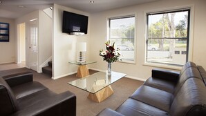 Una sala de estar moderna con una mesa de centro de vidrio, sofás de cuero, un televisor de pantalla plana y un jarrón con flores.