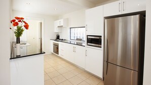 Una cocina moderna con armarios blancos, un refrigerador de acero inoxidable y una ventana sobre el horno.