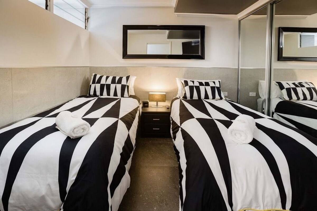 Habitació d'hotel amb dos llits, cadascun amb roba de llit a ratlles negres i blanques, una taula de nit amb una làmpada i un mirall a la paret.