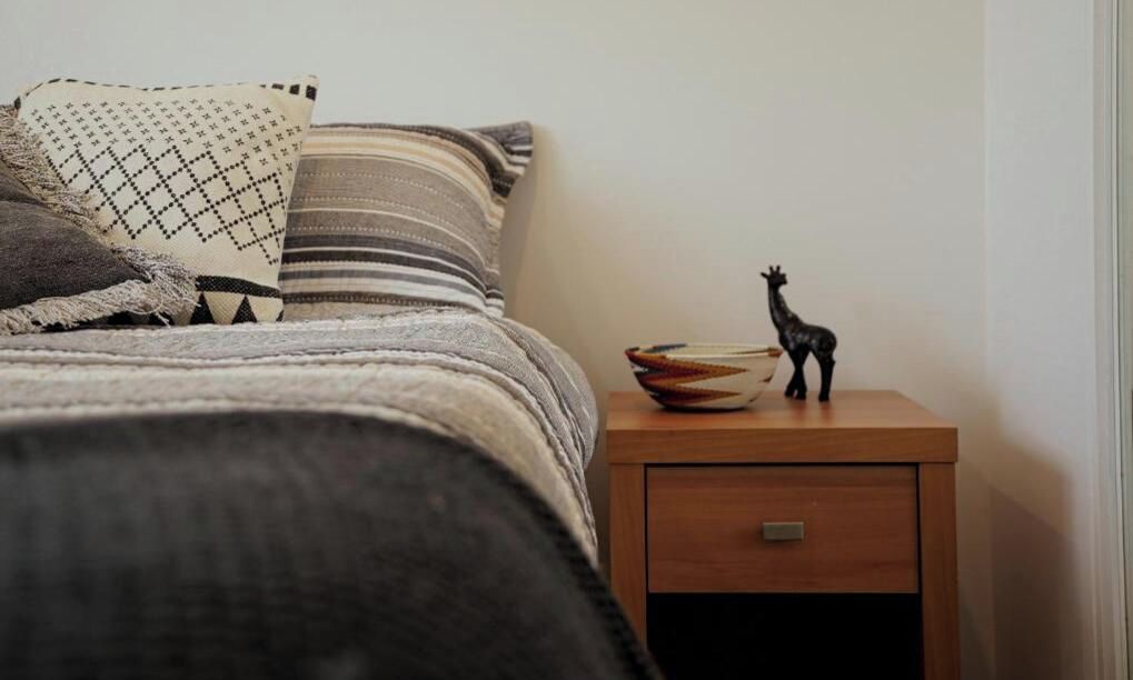 Un lit avec une couverture à rayures et un oreiller, une petite table de chevet en bois avec un tiroir, et une figurine décorative représentant une girafe.