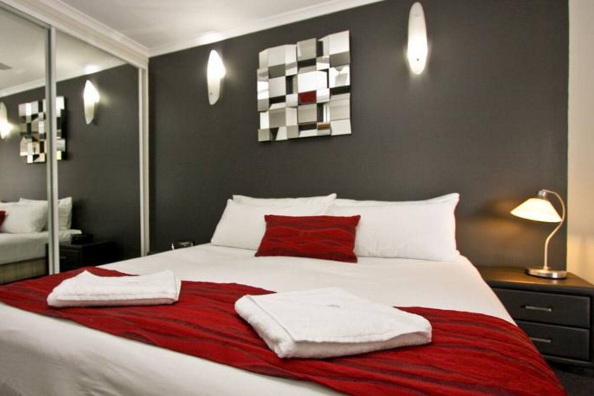 Habitació d'hotel amb un llit gran, un mirall, una obra d'art a la paret i una tauleta de nit amb una làmpada.