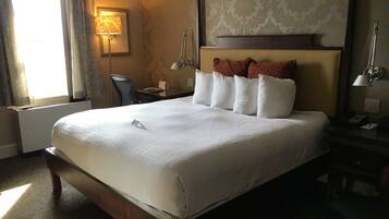 Una camera d'albergo con un letto grande, una scrivania con lampada, una sedia e una finestra con tende.