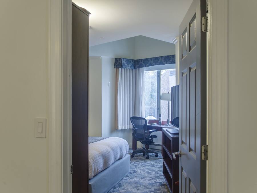 Een hotelkamer met een bed, een bureau met stoel, een raam met gordijnen en een deur.