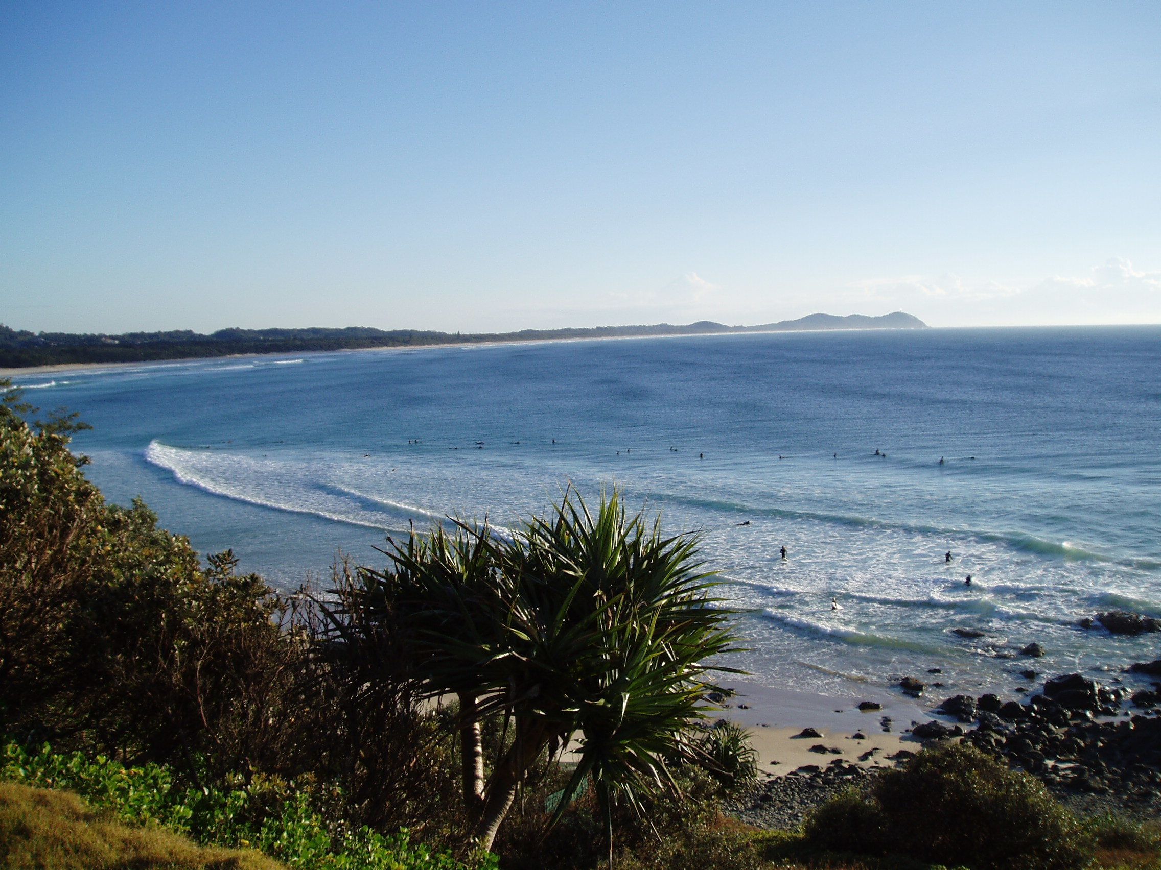 A coastal landscape with a beach, ocean waves, and a distant mountain range.