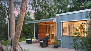 Une maison moderne dotée d’un patio couvert, de deux fauteuils en osier et d’une plante en pot.