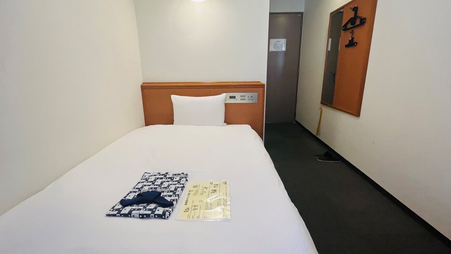 A hotel room with a neatly made bed, a pillow, a folded towel, and a small item on the bed.