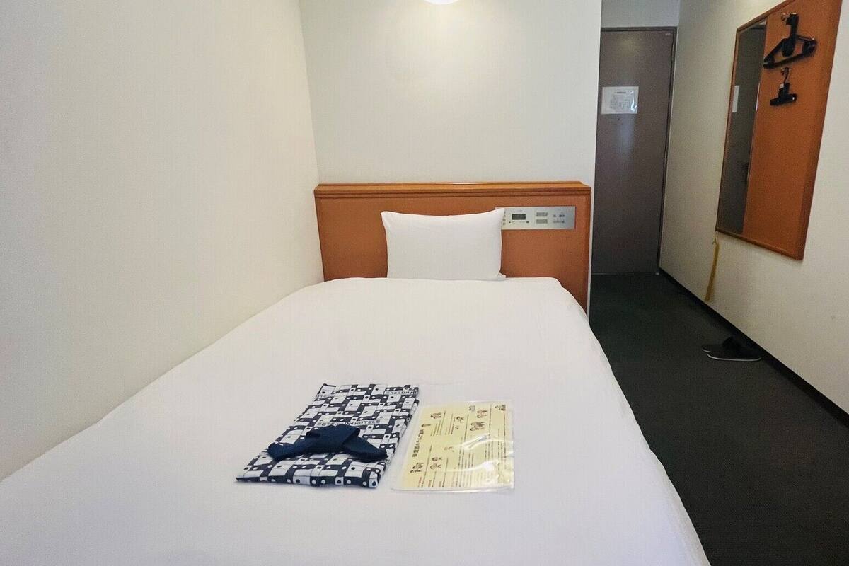 A hotel room with a neatly made bed, a pillow, a folded towel, and a small item on the bed.