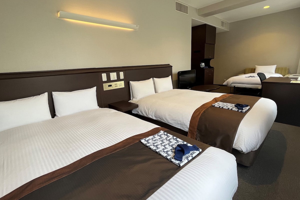 A hotel room with two beds, a desk, a chair, a TV, and a mirror.