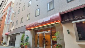 A hotel entrance with a red awning, glass doors, and potted plants outside. - Natural Hot Spring Midosuji Hotel (Osaka)