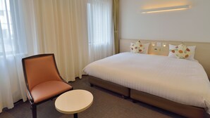 A hotel room with a bed, a chair, a small table, and a window with curtains. - Natural Hot Spring Midosuji Hotel (Osaka)