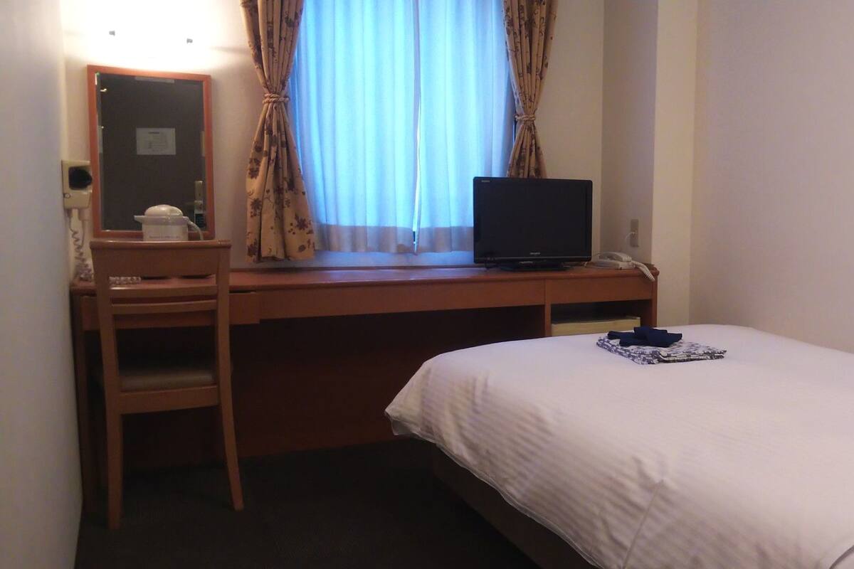 Habitación de hotel con cama, escritorio con computadora, silla y ventana con cortinas.