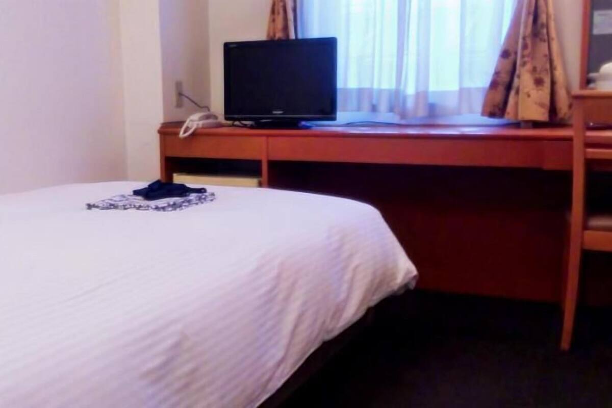 Una habitación de hotel con una cama, un escritorio con monitor de ordenador y un teléfono.