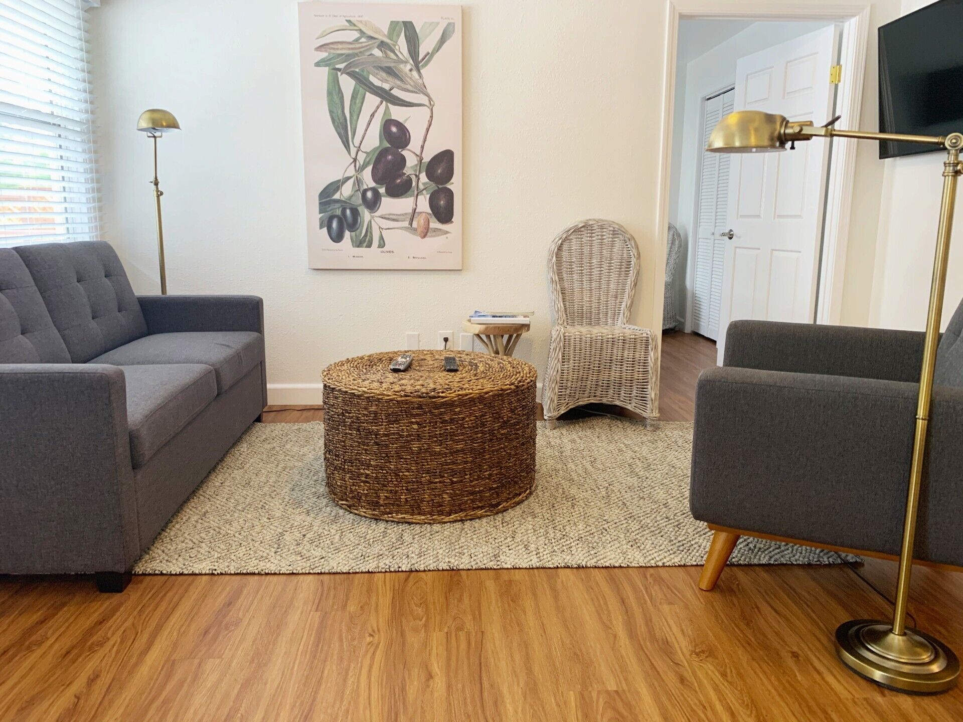 A living room with a grey sofa, a wicker ottoman, a wicker chair, and a floor lamp.