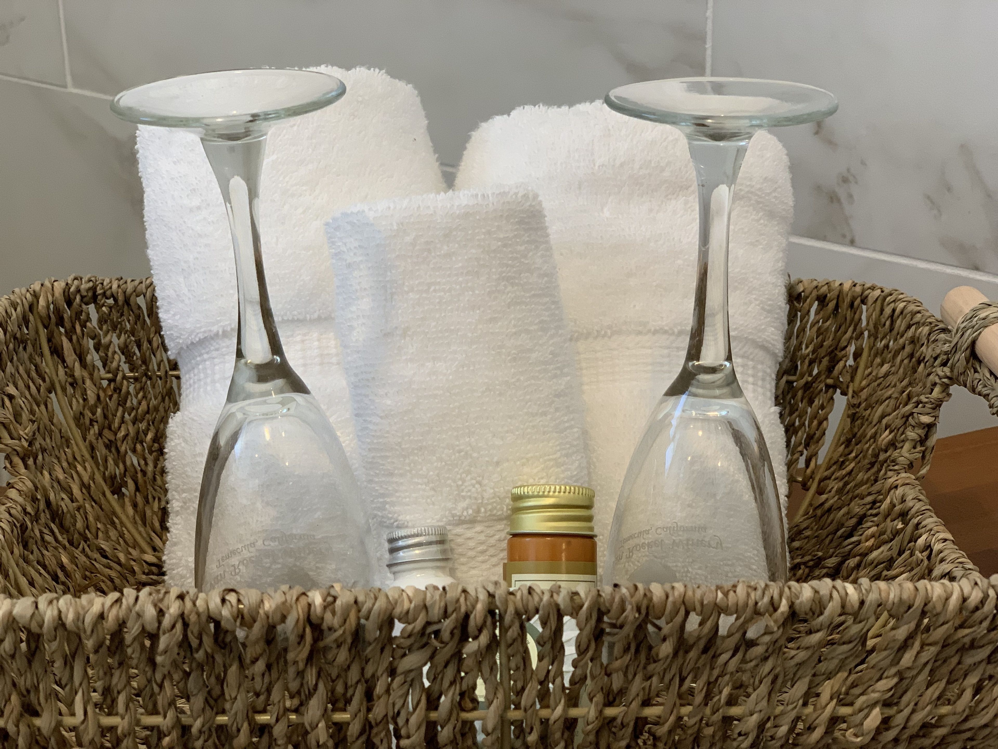 A wicker basket containing two wine glasses, a small bottle, and a white towel.