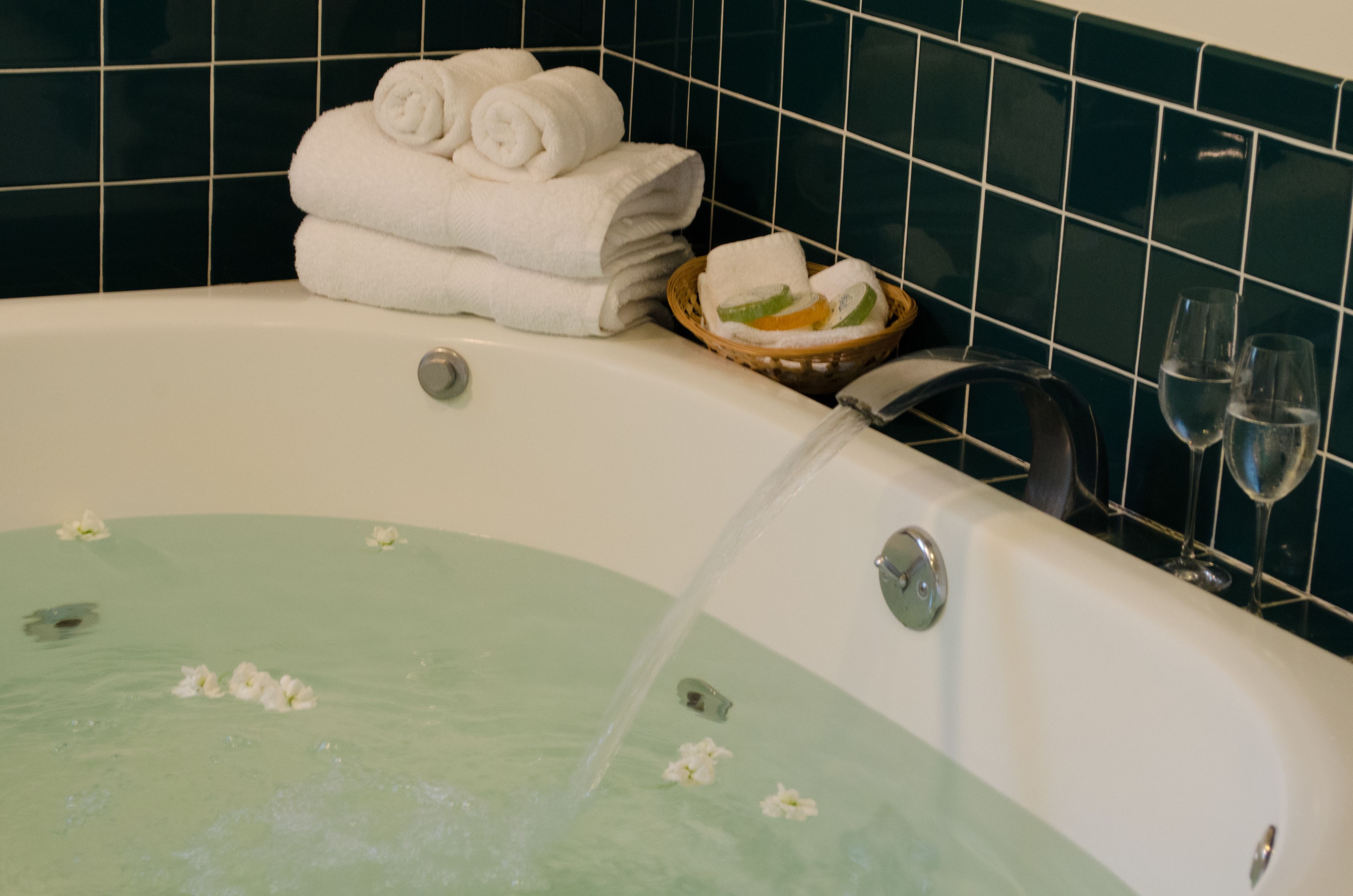 Une baignoire remplie d’eau, une pile de serviettes blanches, un panier rempli de serviettes et deux verres d’eau posés à côté.