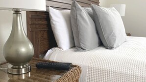 A neatly made bed with a grey and white duvet, a wooden headboard, and a wicker nightstand with a lamp and remote control. - Carlin Cottages (Calistoga)