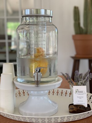 A water dispenser with a measuring gauge, white cups, a small rock, and a sign with a business name and address. - Carlin Cottages (Calistoga)