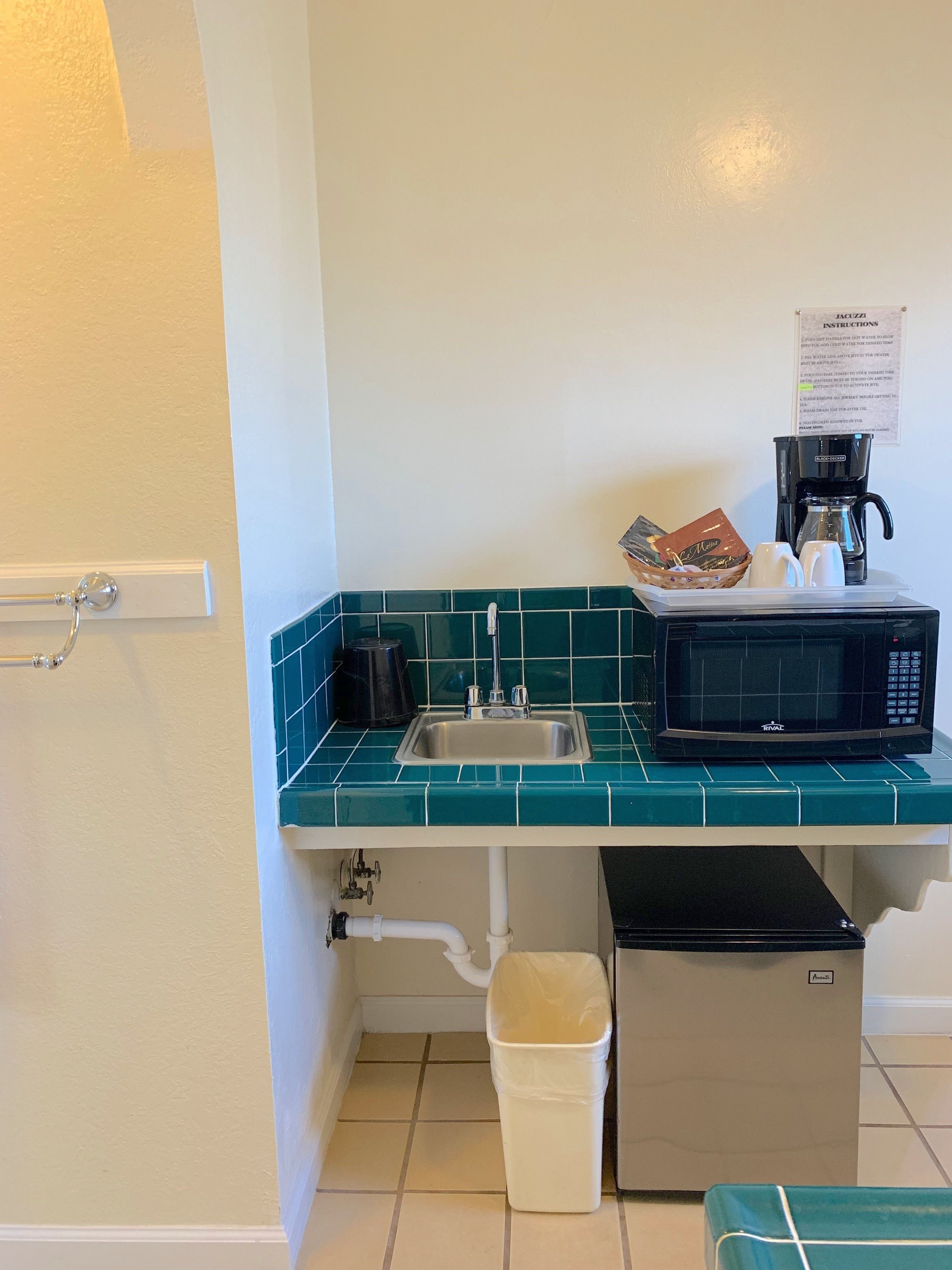 A compact kitchenette with a sink, a coffee maker, a microwave, and a trash bin.