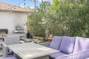An outdoor patio with a grill, wicker furniture, and string lights. - Carlin Cottages (Calistoga)