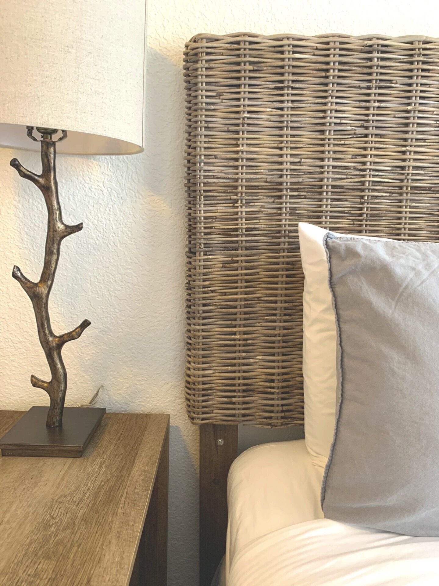 A bed with a grey pillow and a wicker headboard.