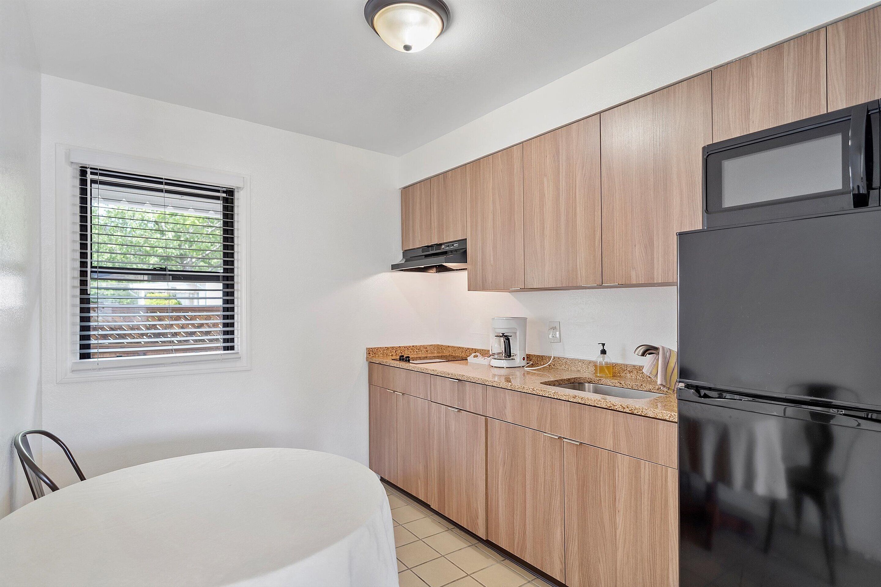 Una cocina moderna con armarios de madera, un refrigerador negro, una cafetera y una ventana con persianas.