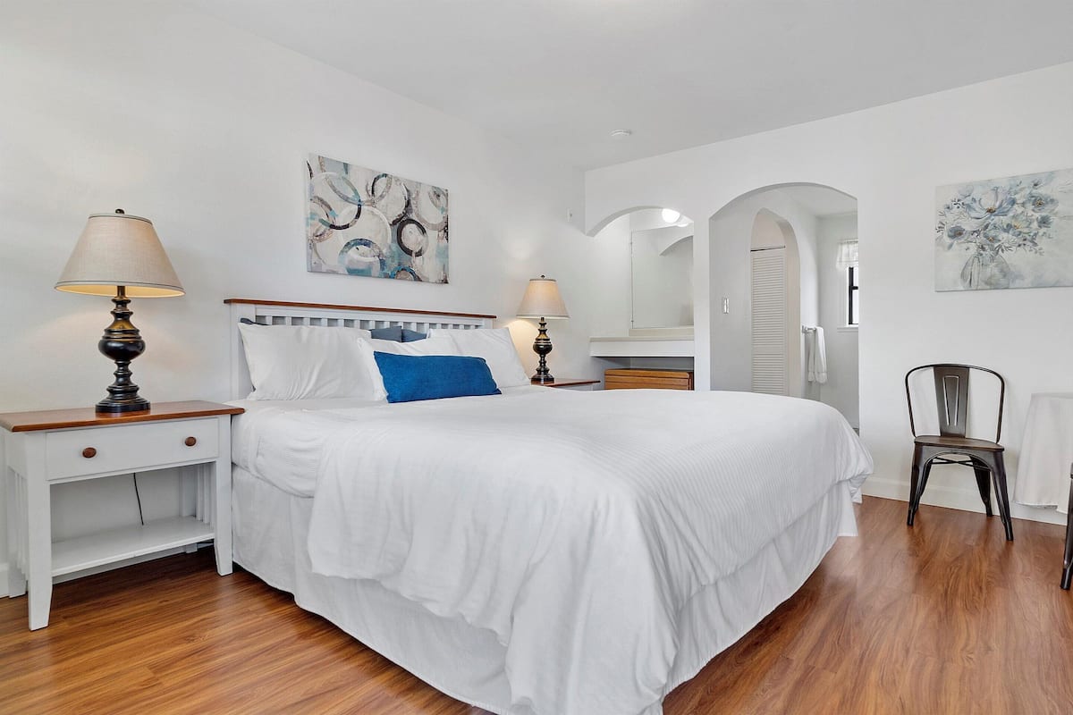 A bedroom with a large bed, two bedside tables with lamps, a chair, and artwork on the walls.