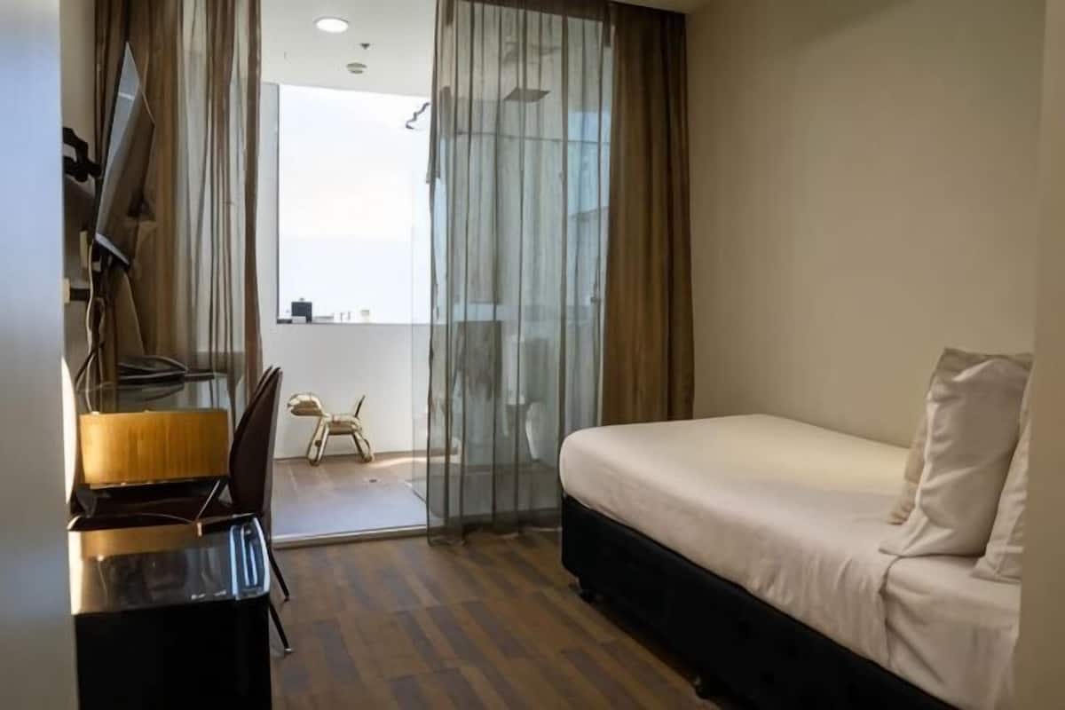 Habitación de hotel con cama, escritorio, silla y vistas a través de un ventanal.
