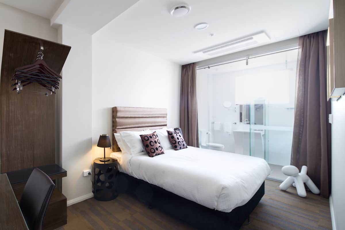 Una habitación de hotel moderna con una cama grande, un escritorio y una zona de ducha de vidrio.
