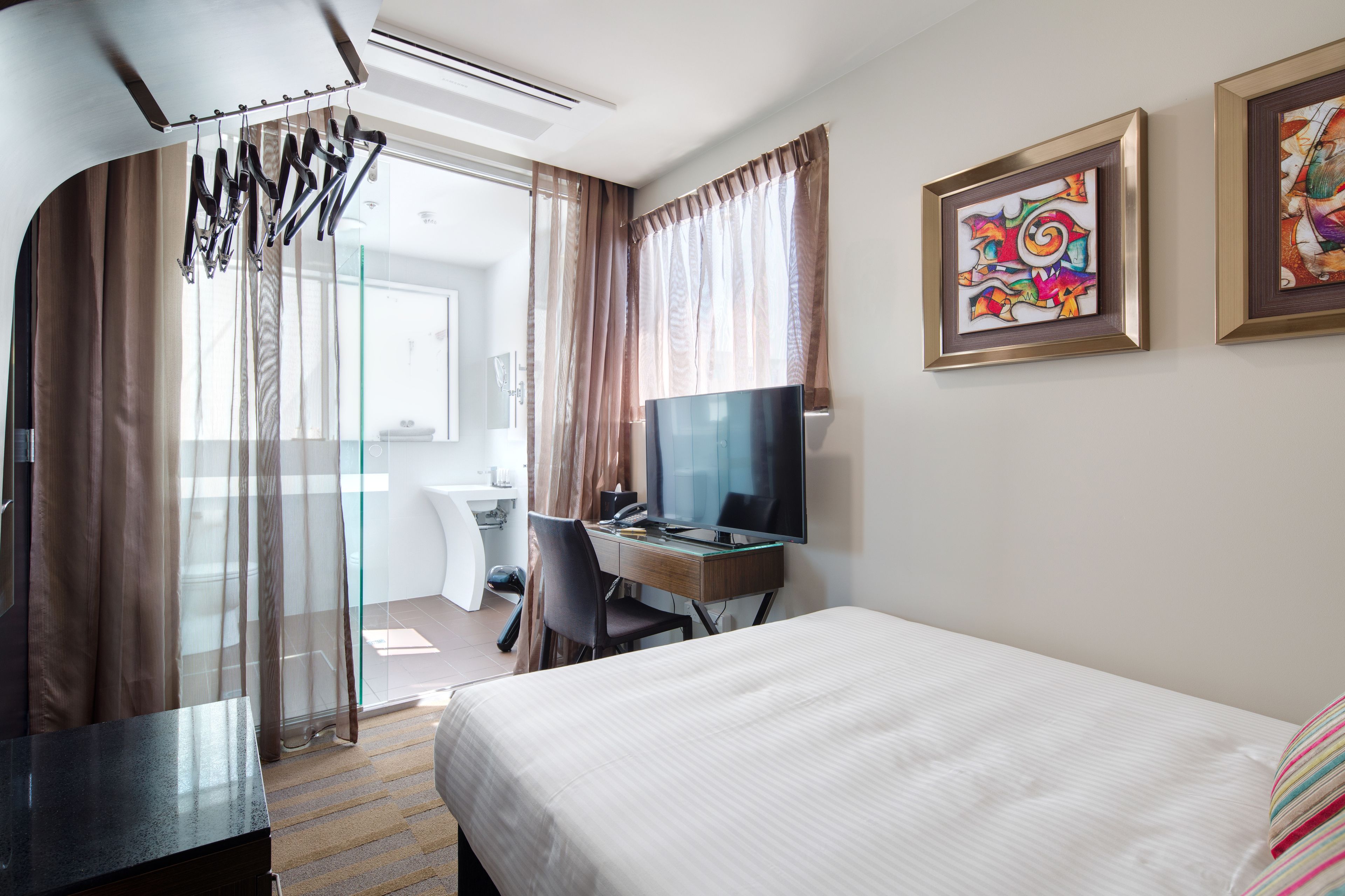 Una habitación de hotel con cama, escritorio con computadora, televisión y zona de ducha.