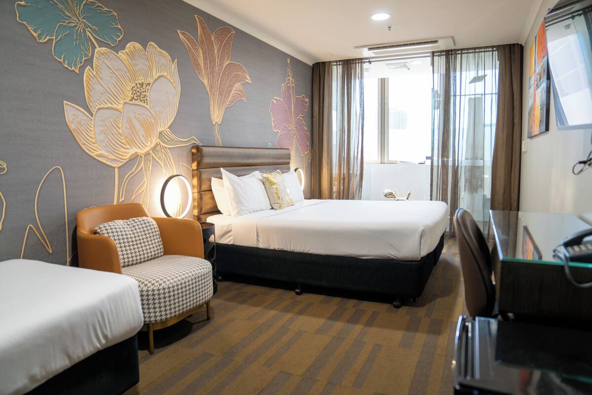Una habitación de hotel con dos camas individuales, un sofá, un escritorio y un ventanal con cortinas.