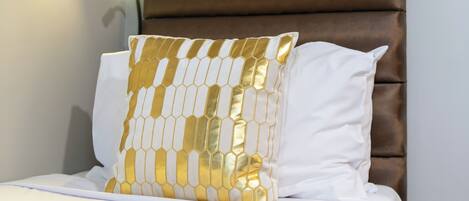 Ein Bett mit braun gepolstertem Kopfteil, weißer Bettwäsche und einem dekorativen Kissen mit geometrischem Muster.