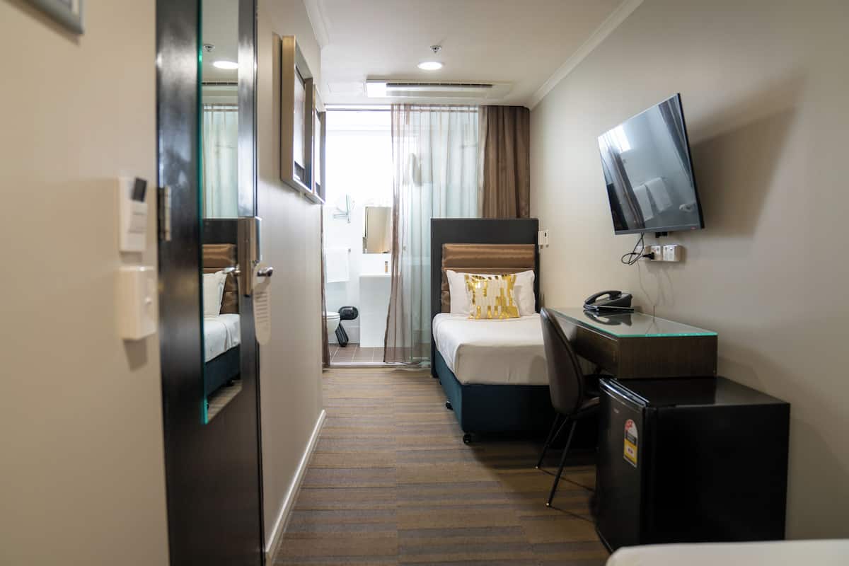 Una habitación de hotel con cama, escritorio, televisor y refrigerador.