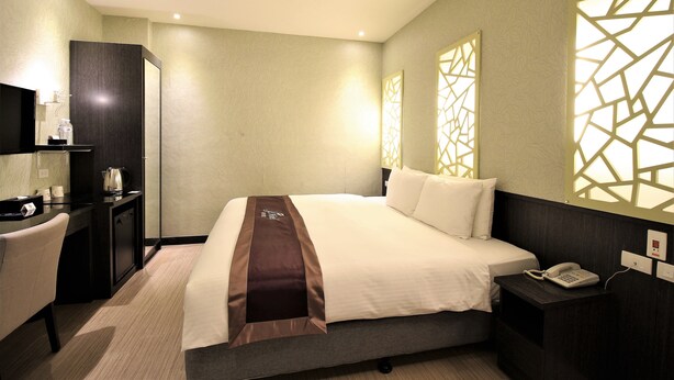 A hotel room with a bed, bedside table with a phone, a desk with a chair, and a TV. - J Hotel (Kaohsiung)