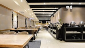Un restaurante moderno con mesas comunes largas, una zona de bufé con mostradores de comida y un interior limpio y bien iluminado.