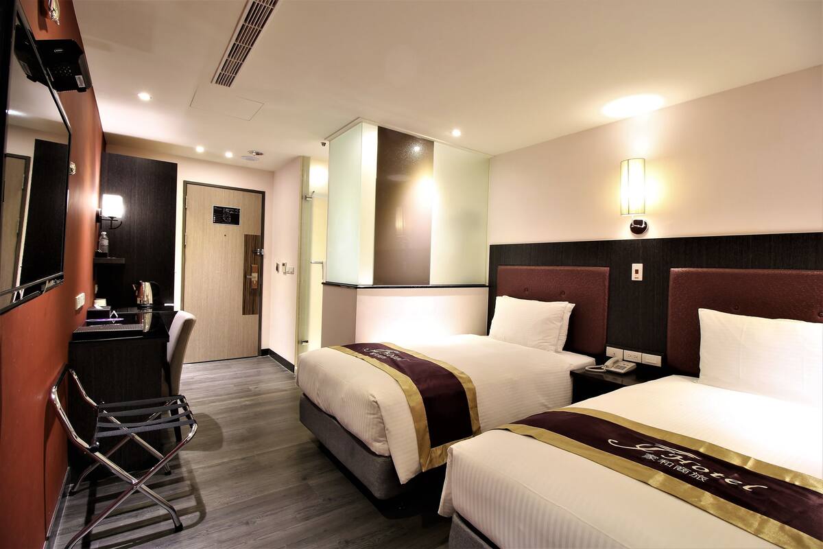A hotel room with two beds, a desk, a chair, and a minibar.