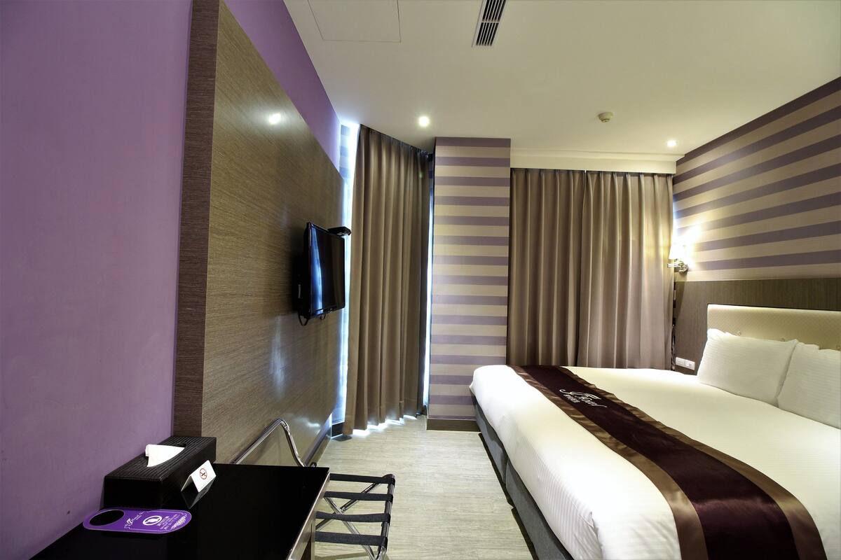 A hotel room with a bed, a desk with a computer, a TV, and curtains.