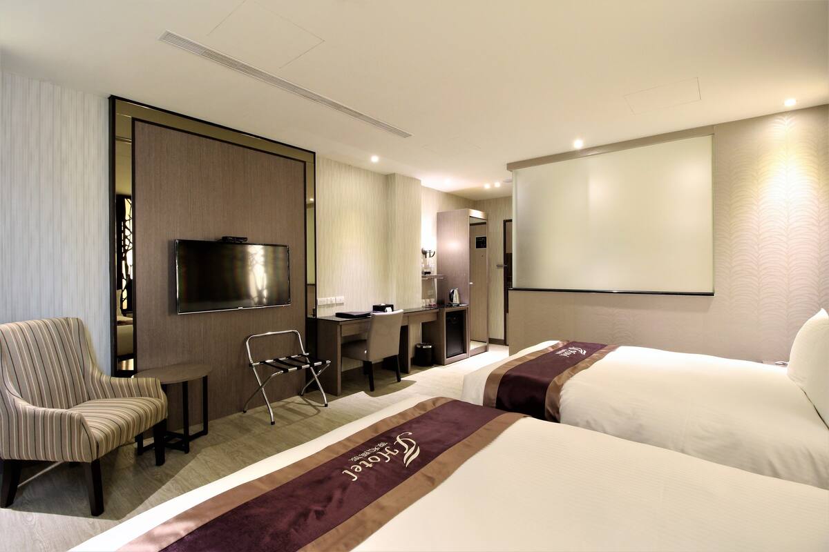 A hotel room with two beds, a desk, a chair, a TV, and a minibar.