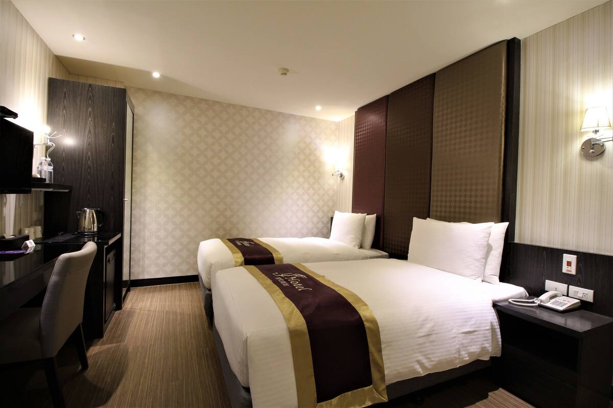 A hotel room with two beds, a desk, and a telephone.