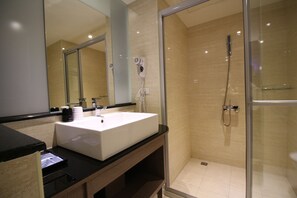 A modern bathroom with a large mirror, a white sink, a hairdryer, and a glass-enclosed shower area. - J Hotel (Kaohsiung)
