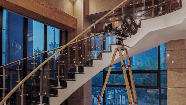 A modern interior with a grand staircase, large windows, and a vintage camera on a tripod. - Jeonju YeongHwa Hotel (Jeonju)