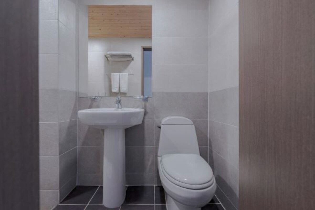 Un bany petit i modern amb un lavabo blanc, un vàter i una prestatgeria de fusta sobre el lavabo.